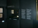 Das Bild zeigt einen Museumsraum mit Vitrinen, die historische Artefakte wie Dokumente und Schreibutensilien präsentieren. An den Wänden befinden sich großformatige Texte in Deutsch und Englisch, die sich mit dem Konzept von "Gewalt" auseinandersetzen, insbesondere im Kontext von Goethes Verständnis von Macht und Gestaltung. 