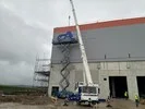 Arbeiter auf Hebebühne montiert großen blauen Schriftzug 