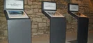 Drei Ausstellungstafeln vor einer Steinmauer mit Texten zu Geschichte und Zerstörung der ehemaligen Synagoge