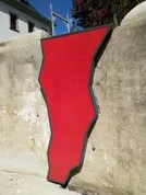 Großes rotes, unregelmäßig geformtes Schild an einer hellen Mauer im Freien